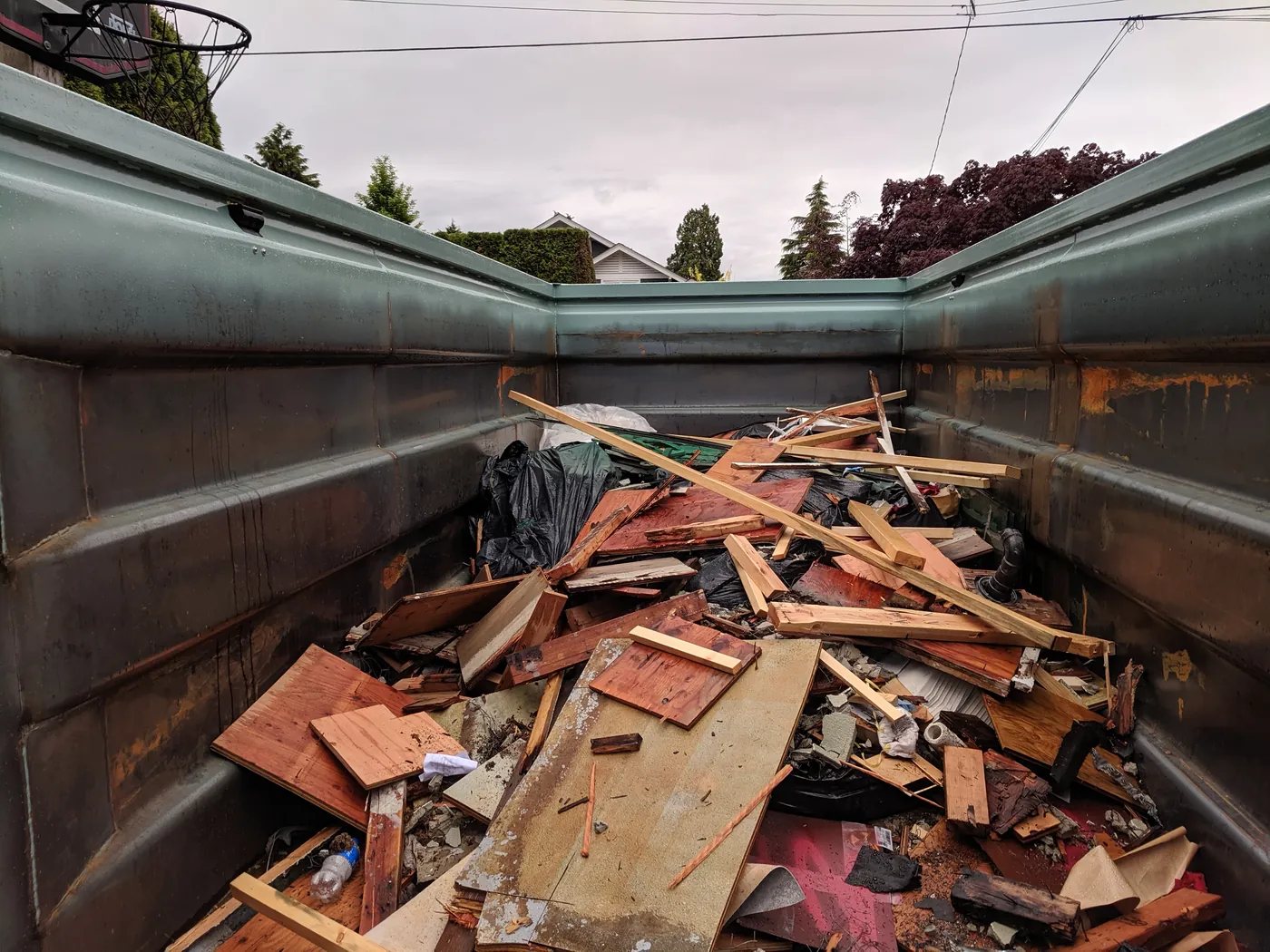 Inside of a construction roll-off bin filled with wood, drywall, and debris, with an iamFull sensor mounted on the rim
